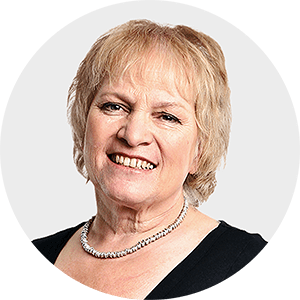 a woman wearing a pearl necklace smiles for the camera